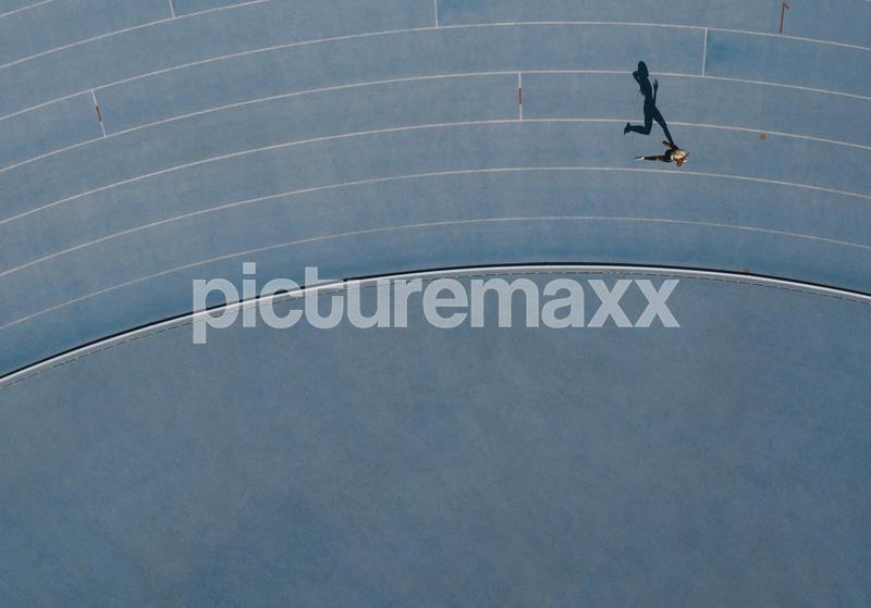 Sprinter running on athletic track. Top view of a sprinter running on race track in a stadium with shadow falling on the side.
