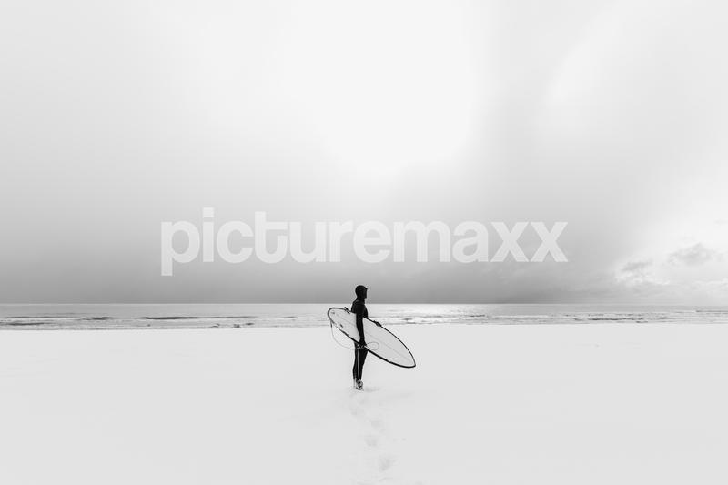 Winter and surfer with surfboard. Snowy beach and surfer in wetsuit.